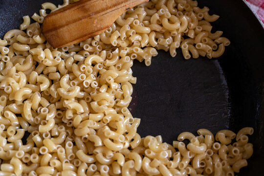 friendo pasta de coditos en sart&eacute;n de tefl&oacute;n con palita de madera