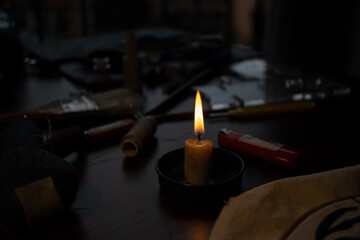 Vela encendida con llama, en una mesa desordenada, usada para encerar hilo