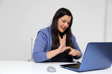 Latino adult woman speaks Mexican sign language with a deaf person through a laptop in a video call
