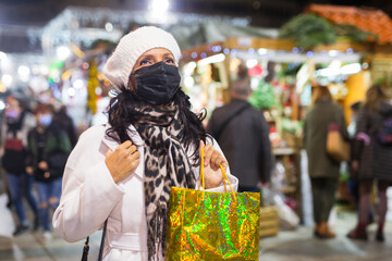 Obraz premium Portrait of a Latin American woman in a protective mask with a paper bag who came to an open-air Christmas fair during the ..pandemic