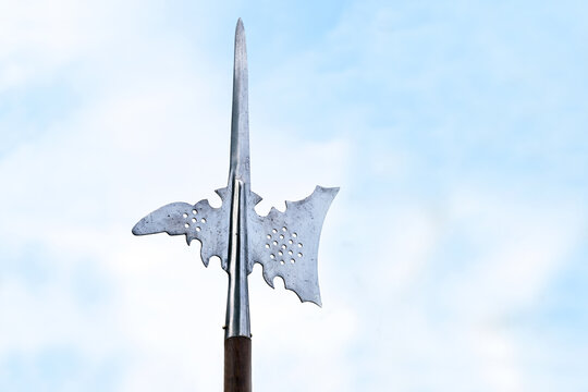 Metal top of a halberd, also called halbard, halbert or Swiss voulge, with axe blade and spike against a cloudy blue sky, pole weapon, copy space
