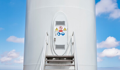 Entrance door at base of wind turbine tower with sign warning of danger to workers - Renewable energy concept.