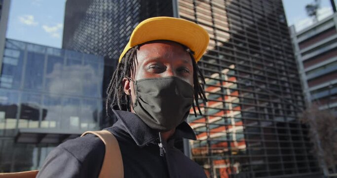 Portrait young black american man walking city sidewalk wearing surgical mask for outbreak prevention. African person walking in urban environment