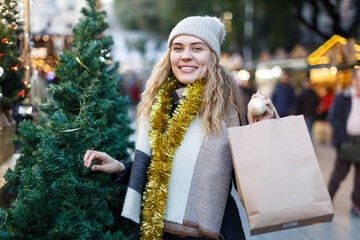 Smiling young woman spending time at fair and buying Christmas tree