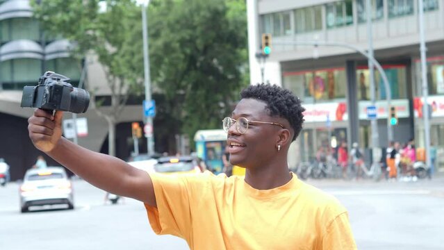  Young African American man recording himself on a video camera in a city. Influencer, traveler, digital content creator