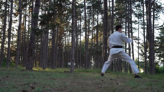 Man training karate in the forest one male athlete karateka caucasian practitioner doing kata in nature in the woods in day real people