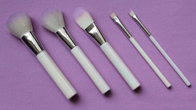 Set de brochas blancas para maquillar en diferentes tama&ntilde;os y acomodadas sobre un fondo morado.
