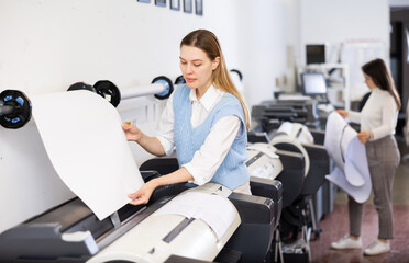 Female print worker controlling printing process on modern offset machine in print shop