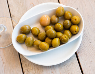 Closeup of plate of pickled green olives with a stone, spanish appetizer