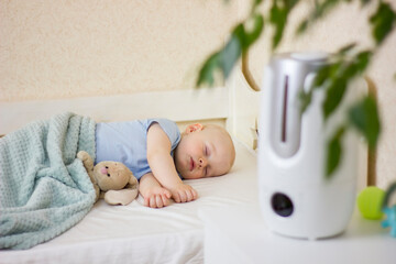 Cute little baby boy sleeping in bedroom with air humidifier.