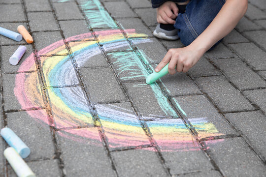 A child drawing a rainbow on the street with colored chalk. Selective focus. Kid. A child is playing outside