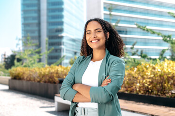 Successful elegant confident young mixed race woman with curly hair, formally dressed, stands...