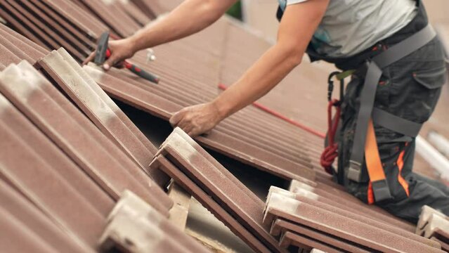 Worker fixing roof by nailing tiles back on roof battens