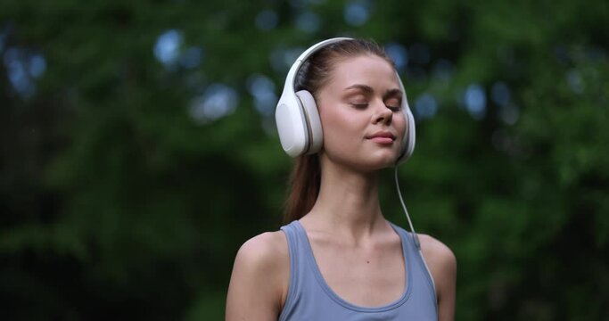 Woman wearing big white headphones listens to her favorite music while exercising in nature and smiles with happiness and lifestyle