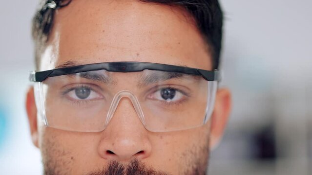 Closeup of male scientist eyes and face wearing safety glasses or goggles for protection from dangerous, hazardous materials. Isolated technician or engineer working in a lab, with bokeh background.