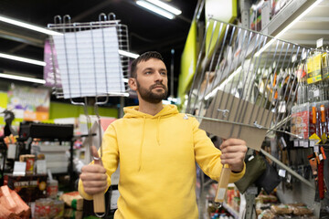 a young man chooses a grill and barbecue for a picnic in a tourism goods store