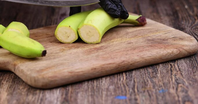 cut into pieces an unripe green banana, a banana with a green peel on the table during cooking