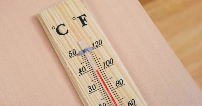 Temperature indicator rises high quickly on wooden thermometer caused by sultriness in room. Thermometer lies on table made of light wood extreme closeup