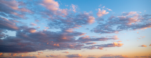 Evening blue sky and gray clouds with orange and pink highlights reflecting setting or rising sun, at dusk or dawn.