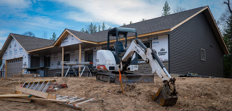 CROW WING CO, MN - 5 MAY 2022: Bobcat mini excavator with skid steer tracks, and ladders sit on dirt in front of a new home construction job site.
