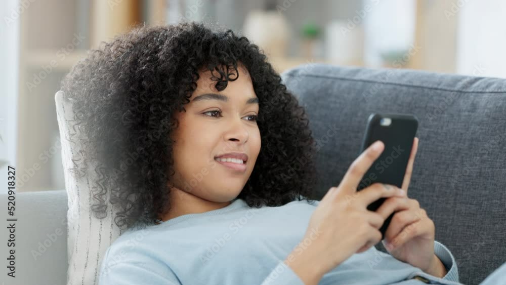 Poster smiling, relaxing female typing on a phone, chatting on social media while lounging on a sofa at hom