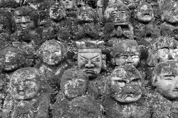 Row of old carved buddha statues in dark forest setting in Arashiyama, Kyoto, Japan