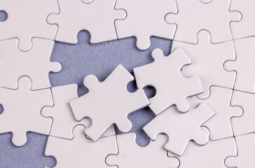 Obraz premium Missing jigsaw puzzle pieces. Business concept. Fragment of a folded white jigsaw puzzle and a pile of uncombed puzzle elements against