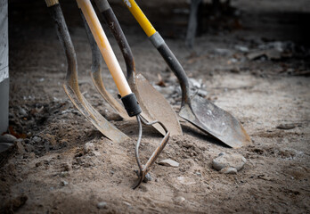 Dirty used shovels and a rake lean against a wall during a work break at a new home construction...