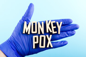 Wooden letters text MONKEYPOX on a doctor's hand in a blue glove. Monkeypox virus concept.