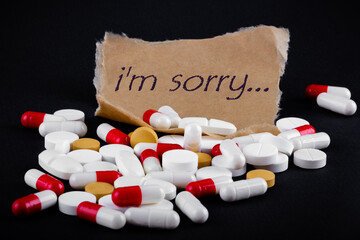 Text I'm sorry on a piece of paper next to a pile of pills. Death note. Suicide concept.