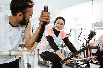 two beautiful woman with hijab and friend at the gym exercising with friend on static elliptical...