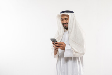 an arabian youth in a turban using a mobile phone wiping the screen while smiling on a plain background