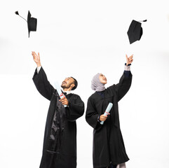 Couple of graduate students wearing black toga holding up a blackboard hat standing on a isolated...