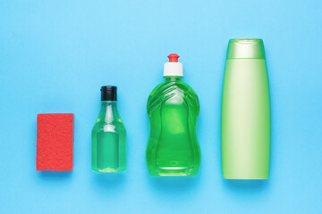 Red foam sponge and green bottles with detergents on a blue background. Cleaning kit.