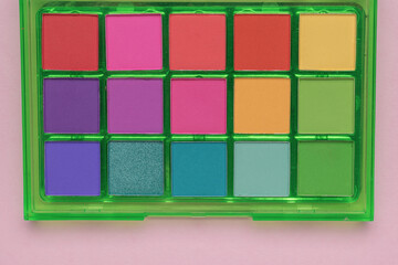A set of multi-colored eyeshadow in a green package on a pink background. Flat lay.
