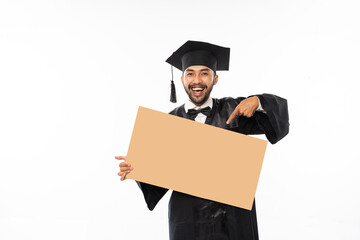 Graduate male students wearing toga holding blank space carton with finger pointing on isolated background - obrazy, fototapety, plakaty