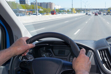  Male hands hold the steering wheel of a car while driving on a highway.