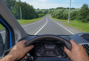 Male hands on the steering wheel of a car on the background of a winding road.
