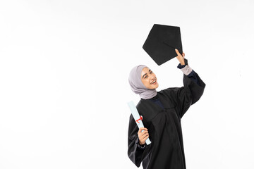 Young graduate Muslim female student in toga holding up black board hat standing on white background