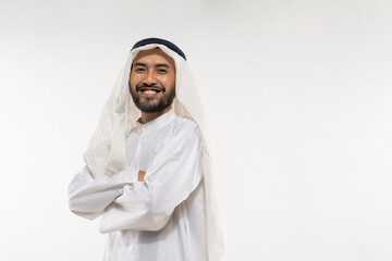 an arabian young man in a turban standing smiling with crossed hands on a plain background
