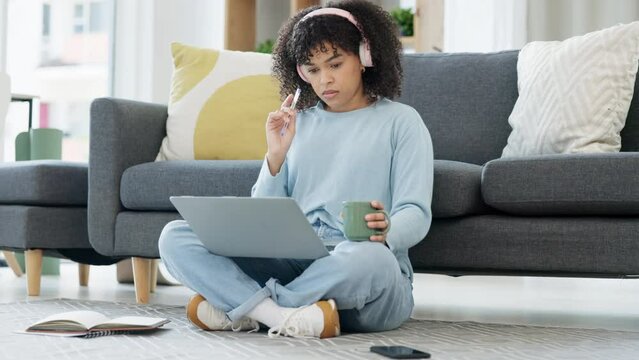 Female university student thinking, working and studying on a laptop, preparing college exams and finals. Young woman listening to music, reading study material online and sitting on the floor