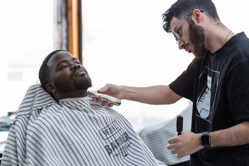 Young handsome bearded african man doing beard haircut in barbershop. Handsome young bearded arfik...