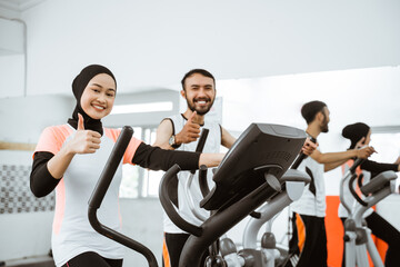 muslim women at the gym doing cardio exercises on static elliptical cycle machine showing thumb up