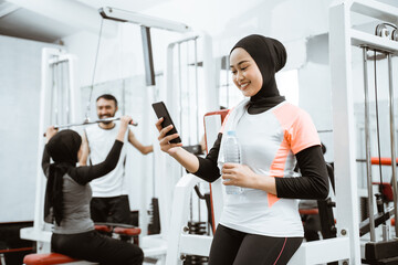 beautiful muslim sporty woman taking a break after exercising at the gym sitting on the floor and using phone
