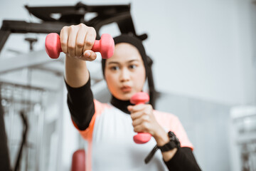 Asian muslim woman doing exercise, lifting dumbbell at the gym
