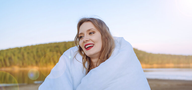 Young woman portrait of a smiling wrapped in a white blanket in the morning on the beach