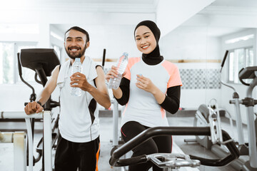 muslim couple exercising together at the gym having a bottle of water while taking a break