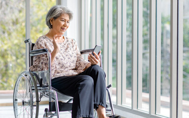 Fototapeta na wymiar Asian happy cheerful old senior healthy gray hair retired pensioner disability handicapped grandmother sitting smiling on wheelchair using touchscreen smartphone surfing browsing social media online