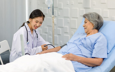 Obraz premium Closeup shot of unrecognizable unknown doctor in white lab coat with stethoscope hand holding comforting supporting old senior unhealthy patient in hospital uniform laying down on bed in ward room