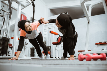 beautiful muslim woman with hijab push up and high five workout together with partner at the gym